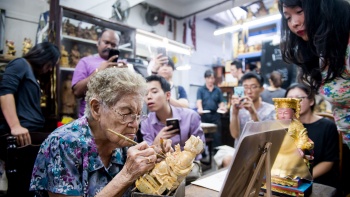Teilnehmer beobachten einen Schnitzermeister im Say Tian Hng Buddha Shop