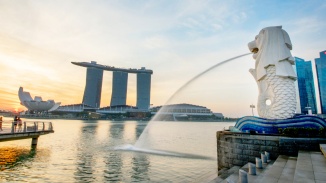Der Merlion speit Wasser in den Singapore River vor dem Hintergrund der Skyline Singapurs am Tag
