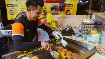 Close up candid shot of a vendor at a <i>pasar malam</i> preparing the famous Ramly burgers over the grill