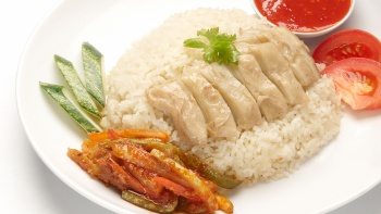 Close up shot of plate of chicken rice with assorted vegetables by the side
