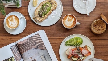 Flatlay image of Avocado Toast, two coffees ,  Classic Salmon sourdough bread topped with herbed cream cheese and a magazine at The Glasshouse Specialty Coffee and Toast Bar Singapore