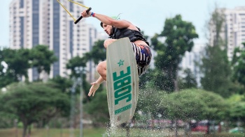 Wake board surfer jumping out of the water at Singapore Wake Park with green city in the background 