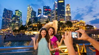 Dua wanita mengambil foto bersama Merlion dengan latar belakang cakrawala Singapura