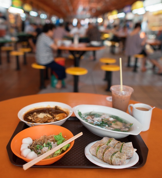 A bokeh shot of hawker food against the backdrop of a hawker centre 