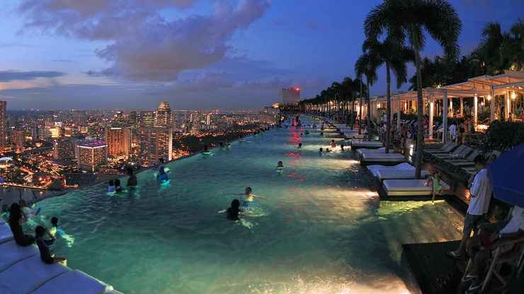 A view of the infinity pool on the Marina Bay Sands SkyPark, overlooking the Singapore skyline at night.