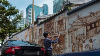 ผู้หญิงคนหนึ่งกำลังถ่ายรูปภาพวาดบนฝาผนัง Thian Hock Keng ตามถนน Amoy 