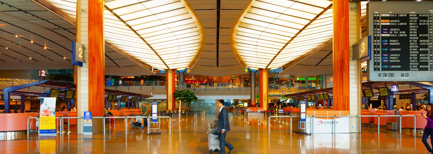 นักเดินทางในชุดสูทพร้อมกระเป๋าเดินทาง กำลังเดินทางผ่านเคาน์เตอร์เช็คอินสัมภาระและเคาน์เตอร์ออกบัตรโดยสารใน Singapore Changi Airport