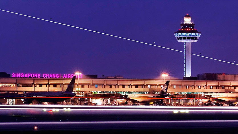 Pesawat di landasan pacu Changi Airport dengan menara pengawas di latar belakangnya