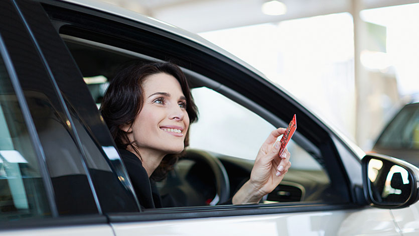 A lady holding her card, whilst looking out of the car