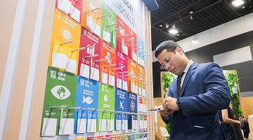 Man taking notes at Urban Solutions World Cities Summit banner displaying sustainable development goals in a conference hall.