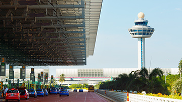 Airport taxi queue under a roof, with control tower and terminal in view; inspires eco-friendly events.
