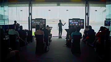 Speaker at conference hall during Deloitte Management Retreat, with virtual and in person attendees.