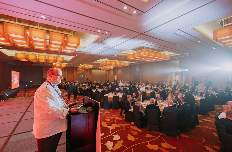 Chef on podium takes query while group of people dine at round table during WCC 2024.