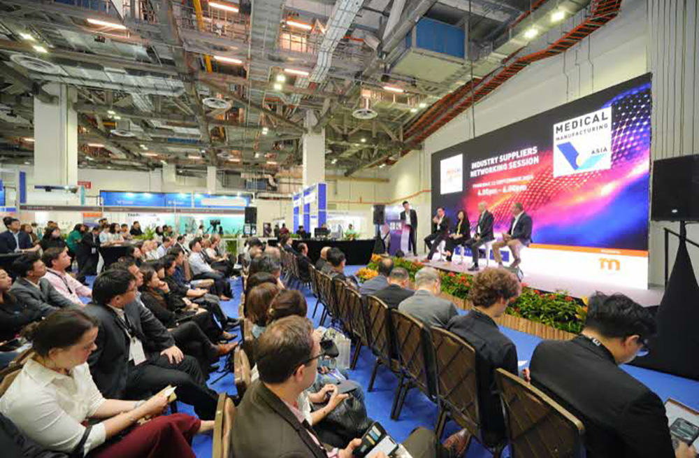 Audience at a medical manufacturing event with speakers discussing industry topics.