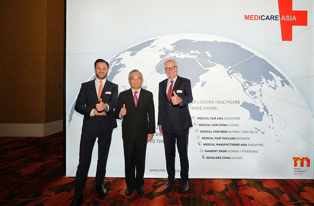 Three people smiling and giving thumbs up in front of a world map with 'MEDICARE ASIA,' symbolizing growth in healthcare.