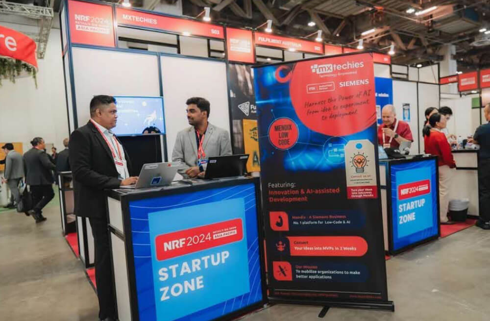Two men chat at a tech startup booth, surrounded by banners and displays at NRF 2024: Retail’s Big Show.