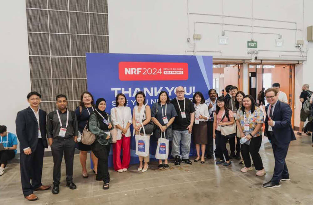 A group poses indoors by a NRF 2024: Retail’s Big Show Asia Pacific sign