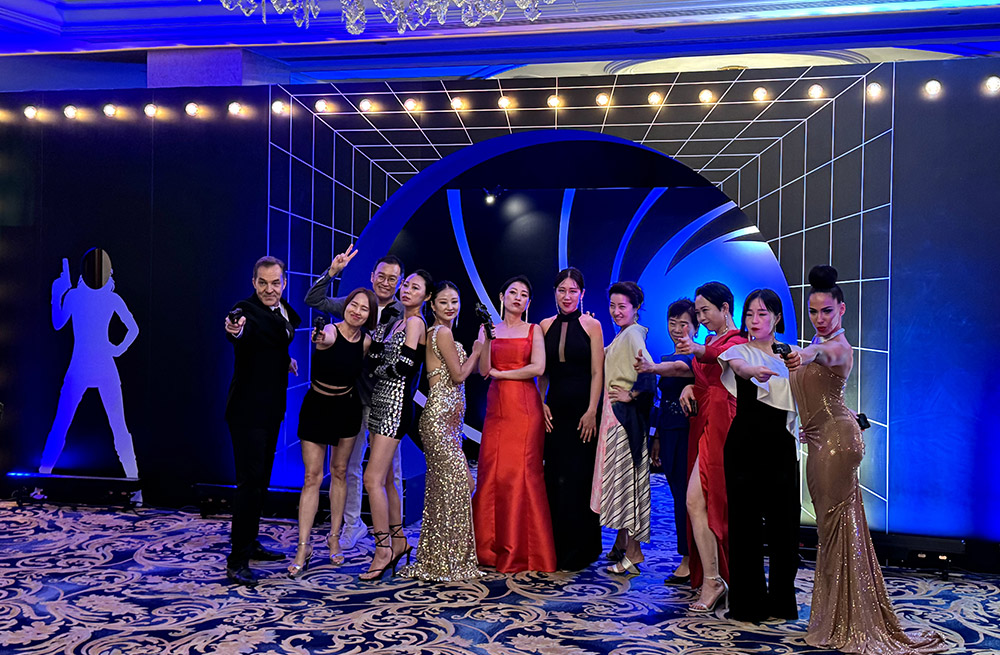 A lively group in formal wear strikes playful poses at the 2024 James Bond-themed Nu Skin Korea dinner event in Singapore.