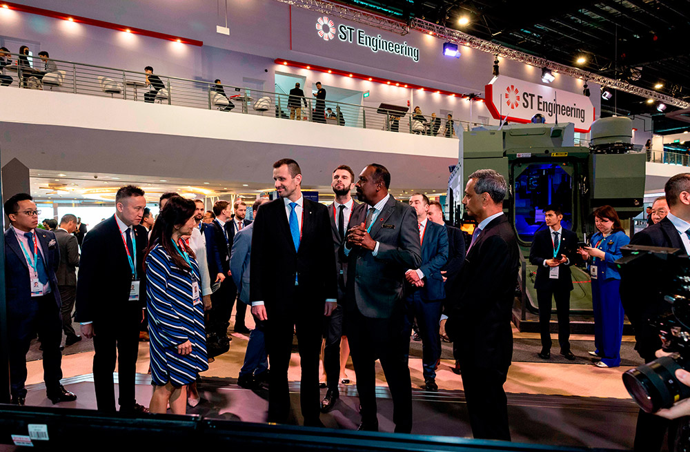 Men and women greet each other at Singapore Airshow 2024 with group of people behind them at exhibition hall.