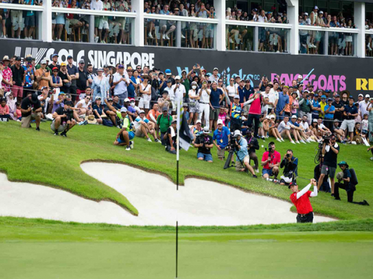 Golfer hitting a bunker shot at the LIV Golf Tournament in Singapore, with a crowd of spectators watching.