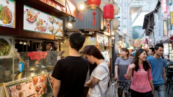 Menschen schauen sich die Speisekarte an einem Imbissstand in der Chinatown Food Street an.