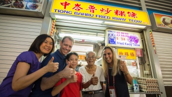 Besucher posieren mit hochgereckten Daumen vor einem Fried Kway Teow-Imbissstand in Tiong Bahru 