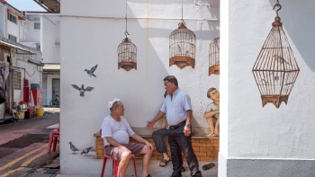 Zwei Männer unterhalten sich am Wandgemälde „Bird Singing Corner“ in der Seng Poh Lane in Tiong Bahru