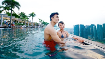 Ein Paar im Infinity-Pool im Marina Bay Sands<sup>®</sup>SkyPark, das sich die Skyline von Singapur bei Tag ansieht
