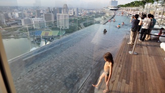 Tagaufnahme von Menschen, die im Sands SkyPark Pool schwimmen und von Besuchern, die Fotos machen