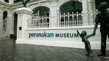 Skulptur eines kleinen Kindes an der Hand eines älteren Mannes vor dem Peranakan Museum