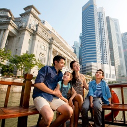 Junge Familie schaut von einem Bumboat aus auf den Singapore River, mit dem Fullerton Hotel im Hintergrund