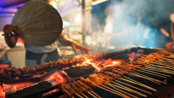 Nahaufnahme eines Manns, der den Satay-Grill anfacht 