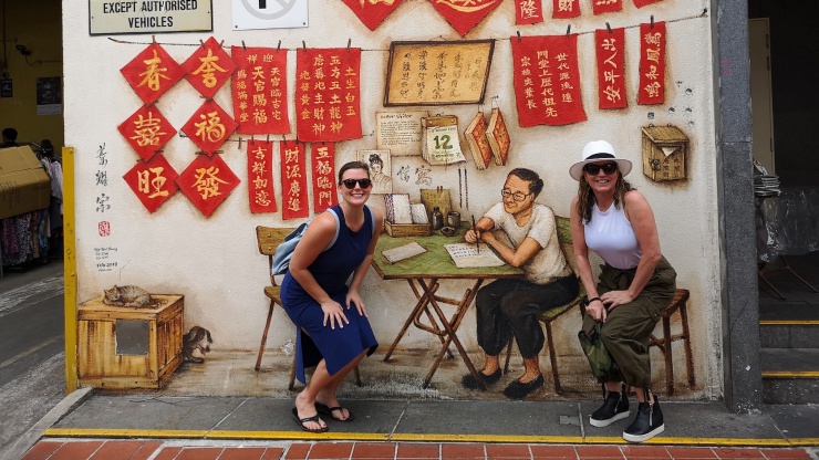 Wandgemälde „Letter Writer“ von Yip Yew Chong (mit zwei Touristen davor)