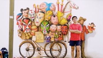 Der lokale Wandmaler Yip Yew Chong posiert neben seinem Wandbild in der Mohammed Ali Lane, das Straßenmaskenverkäufer zeigt