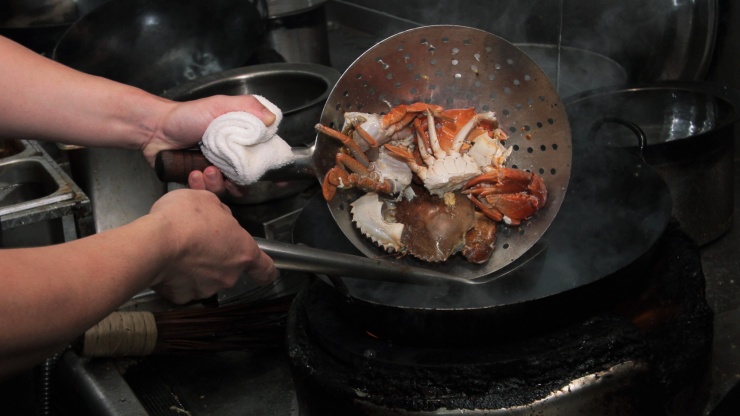 Chef cooking chilli crab in a wok.