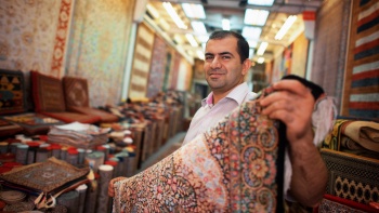 A carpet seller holding up Persian carpet sold at his store