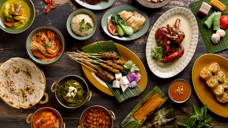 Flat lay of local spread including satays, otah, poh piah, chicken rice, Peranakan kuehs and more.