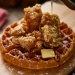 Fried chicken topped on a whole waffle drizzled with syrup and a slice of butter