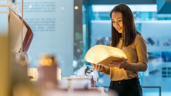 Lady museum visitor at Red Dot Design Museum observing a lamp in the form of a hard cover book