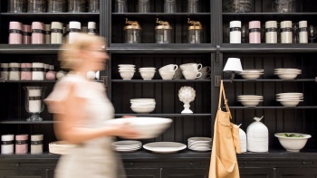 A display of kitchenware with a woman walking by. 