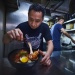 Portrait shot of an owner from A Noodle Story garnishing a bowl of wanton noodles