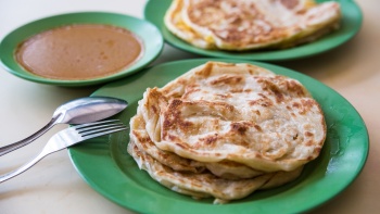 Two plates of roti prata with a side of curry
