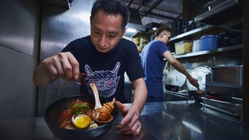 Portrait shot of an owner from A Noodle Story garnishing a bowl of wanton noodles
