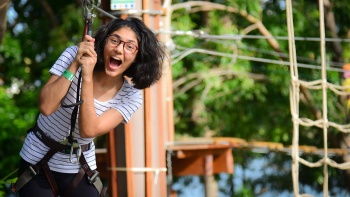 A lady smiling while taking a high element obstacle at Forest Adventure