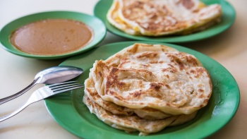 Two plates of plain and egg <i>roti prata</i> with a side of curry.