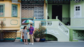 A couple standing under an umbrella in front of Katong shophouses