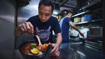 Two chefs at A Noodle Story preparing up a Michelin Bib Gourmand-awarded noodle dish that fuses Japanese ramen with prawns, roast meat and dumplings.