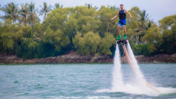 Man jumping out of the water with a jet blade with green bushes in the background 
