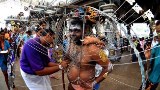 An Indian man assisting another to dress up in the symbolic skewers for Thaipusam procession.