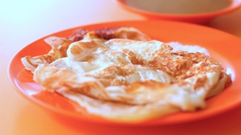 Sepiring roti prata dan kari di latar belakang